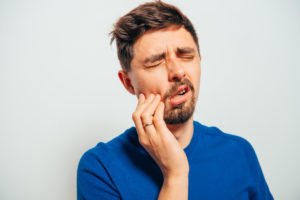 Very nice guy with dark hair holding mouth in pain